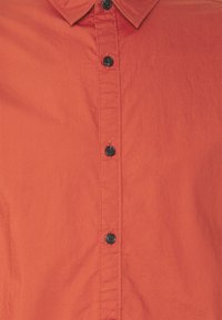 Camisa roja de botones elaborada con tela ligera, que presenta un cuello puntiagudo, botones negros y una textura suave.