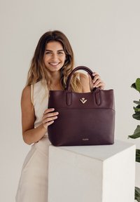 Dunkelburgunderfarbene Lederhandtasche mit robusten Obergriffen, goldenen Beschlägen und geprägt Logo der Marke. Glatte Textur mit klaren Designlinien.