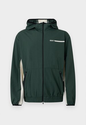 Veste coupe-vent à capuche vert foncé avec un léger motif en grille, fermeture éclair avant, poches zippées, ourlet et poignets élastiques, et panneaux blancs sur les côtés.