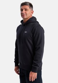 Black hooded sweatshirt with a kangaroo pocket, drawstring neck, and logo patch; made from soft fabric, featuring ribbed cuffs and hem.