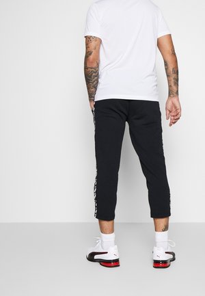 Schwarze Jogginghosen mit weißen Seitenstreifen, kombiniert mit einem weißen T-Shirt und weißen Sneakers. Verfügt über eine schmal zulaufende Passform und einen elastischen Bund.