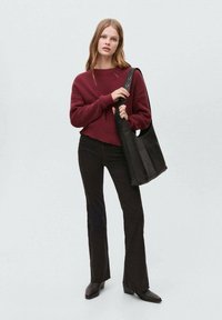 Pulover tricotat burgundy, pantaloni negri evazați și o geantă texturată neagră cu curea pentru umăr. Încălțămintea fină și bine structurată completează ținuta.