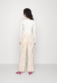 Top branco de manga longa com costuras contrastantes, combinado com calças largas de padrão ondulado multicolorido e sandálias de salto altas rosas.