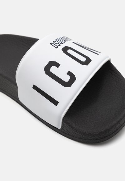 Sandalo slide nero con suola nera testurizzata e strap bianca, caratterizzato da lettering nero in bold che recita "ICON" e il nome del marchio "DSQUARED2."