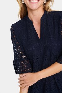 Mekko, jossa on syvä V-pääntie ja lyhyet kellohihat, on tummansinistä pitsiä. Kankaan tekstuuri esittää kukka-aiheita ja monimutkaisia yksityiskohtia.