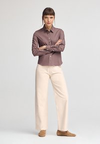 Camicia a maniche lunghe, con bottoni, in tessuto mauve; abbinata a pantaloni larghi di colore crema e scarpe brown slip-on. Design semplice e pulito.