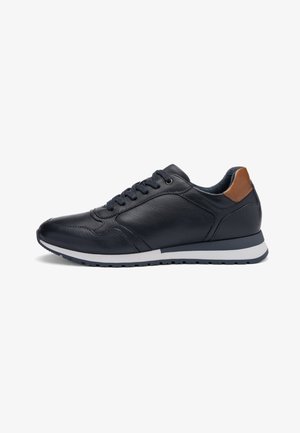 Schwarzer Ledersneaker mit braunem Fersenriemen, schwarzen Schnürsenkeln und weißer Sohle, von der Außenseite auf weißem Hintergrund dargestellt.