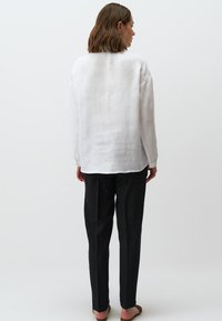 Witte linnen blouse met een ontspannen pasvorm en lange mouwen, gecombineerd met zwarte tapering broek. Gladde textuur; minimalistisch ontwerp.