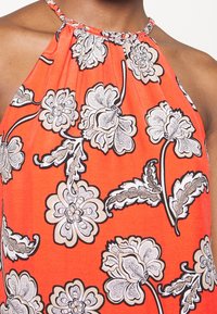 Femme portant un haut dos nu orange vif à larges imprimés floraux blancs et noirs.