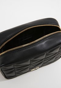 Borsa cosmetica in pelle nera con texture trapuntata, zip dorata e apertura superiore che mostra un interno scuro. Forma rettangolare compatta.