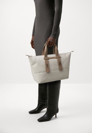 Sac fourre-tout en tissu beige clair avec un motif texturé en grille, doté de deux poignées marron et de subtils accents métalliques.