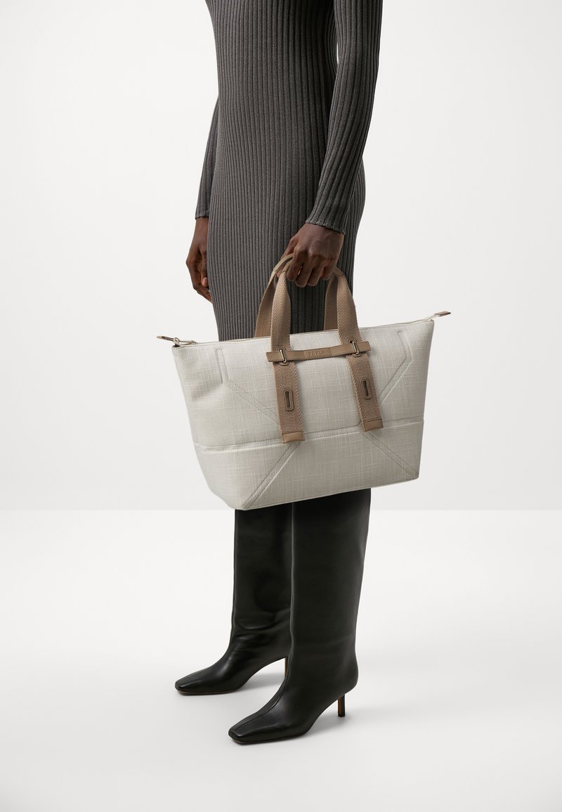 Tote bag in lichtbeige stof met een gestructureerd ruitpatroon, voorzien van dubbele bruine handvatten en subtiele metalen accenten.