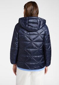 Granatowa kurtka puchowa z kapturem, z diamentowym wzorem, błyszczący materiał i elastyczne mankiety, noszona na jasnoniebieskiej koszuli.