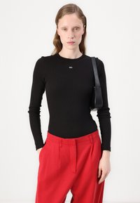 Mustat pitkähihaiset ribbimäiset bodysuitit, joissa on pieni logo rinnassa, yhdistettynä löysiin punaisiin housuihin. Sileä pinta, istuva muotoilu.