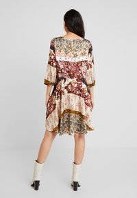Sukienka w kwiatowy wzór w kolorach kremowym, bordowym i brązowym, z rękawami do trzech ćwiartek i rozkloszowanym dołem. Posiada wycięcie w kształcie łezki na plecach oraz fakturowany materiał.