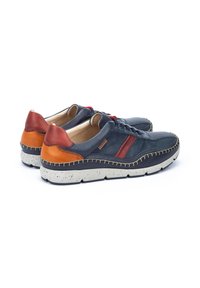 Sneaker in pelle blu navy con dettagli marroni, particolare rosso, pannelli perforati e suola maculata. I punti di cucitura lungo il bordo conferiscono texture.