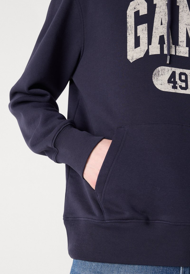 Felpa navy in misto cotone, con tasca a marsupio, polsini a costine e stampa grafica sbiadita. Texture morbida con vestibilità rilassata.
