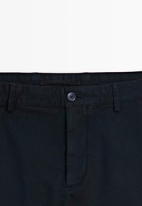 Ceinture de pantalon noire avec un bouton et des passants pour ceinture, présentée sur un fond blanc.