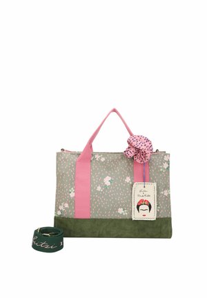 Grüne und pinke Blumen-Tasche mit pinken Griffen, einer pinken Stoffblume, einem Frida-Kahlo-Etikett und einem abnehmbaren grünen Riemen mit pinker Schrift.