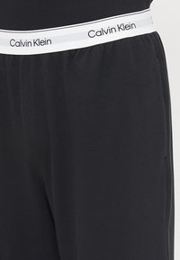 Zwarte joggers met een elastische tailleband, voorzien van een witte band waarop "Calvin Klein" is gedrukt. Zachte stof met een gladde textuur.