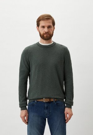 Pullover di maglia verde con texture e colletto rotondo. Presenta polsini e orlo a costine. Indossato con jeans in denim blu e una cintura marrone.