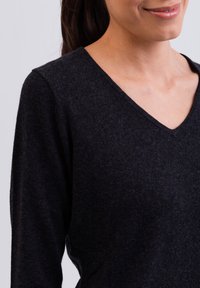 Maglione lavorato a maglia grigio scuro con scollatura a V e maniche lunghe. La trama appare morbida e leggermente pelosa, indicando un materiale accogliente.