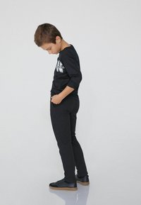 Černá košile s dlouhými rukávy a bílým grafickým designem, spárovaná s úzkými černými kalhotami a černými teniskami s gumovou podrážkou. Jednoduchý, moderní vzhled.