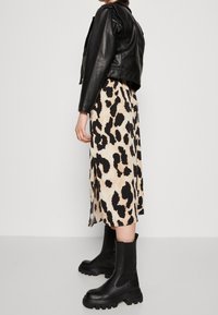 Chaqueta de cuero negra sobre un vestido beige con estampado de leopardo negro, combinada con botas negras de tobillo gruesas. Materiales lisos y texturizados.