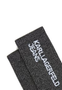 Črn pleten šal z teksturirano površino in belim logotipom "KARL LAGERFELD JEANS", pravokotne oblike in z nezaobljenimi robovi.