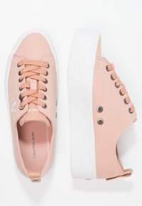 Rosa kanvassneakers med vit gummisula, rund tå och snörning. Har metalldetaljer och en ögla baktill.