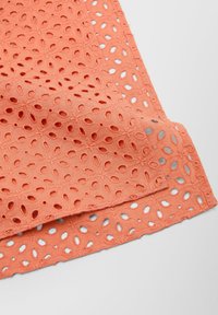 Koraalkleurige stof met een bloemen oogletpatroon en uitsparingen. De randen zijn afgewerkt en de textuur lijkt zacht en lichtgewicht.