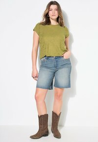 Vihreä oliivi teksturoitu t-paita, siniset farkkushortsit ja ruskeat cowboy-kengät. Shortsit ovat polvimittaiset ja niissä on repsottava helma.