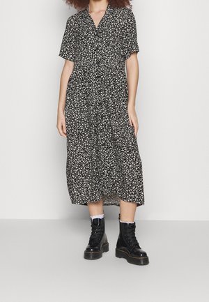 Woman wearing a black midi dress with white floral print and short sleeves, paired with white socks and black lace-up combat boots.