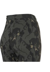 Pantalon vert foncé avec un motif floral noir et beige, montrant la ceinture et la couture latérale sur fond blanc.