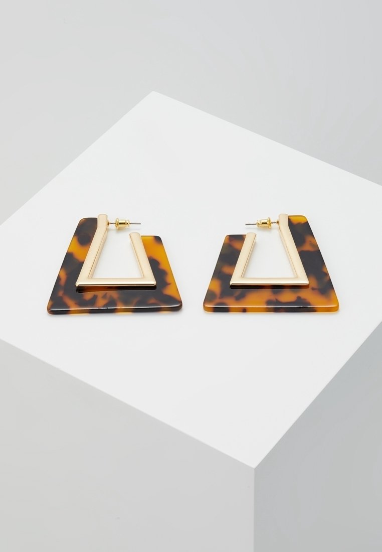 Paire de boucles d'oreilles triangulaires au motif écaille avec de petits cadres triangulaires dorés à l'intérieur, posées sur une surface blanche.