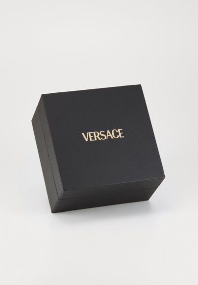Melnā taisnstūra kaste ar teksturētu apdari, uz kuras augšpuses ar zeltītu krāsu ir drukāts "VERSACE". Augstas kvalitātes iepakojuma dizains.