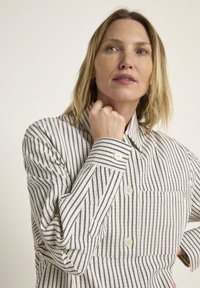 Button-up shirt made of lightweight fabric with vertical blue and white stripes, a collar, and a chest pocket for added detail.