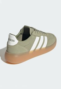 Zeleni teksturirani gornji dio cipela s bijelim prugama i logotipom na peti, s prozirnim svijetlosmešnim đonom. Klasičan dizajn s vezicama.