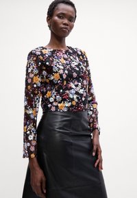 Zwarte top met lange mouwen en bloemenborduursels in verschillende kleuren, gecombineerd met een zwarte leren rok, met een aansluitend ontwerp en een gladde textuur.