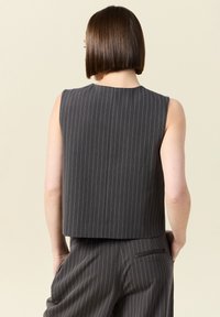 Grå randig ärmlös topp med en fyrkantig skärning, som har en solid tygtextur och en söm på baksidan, bärs tillsammans med matchande randiga byxor.