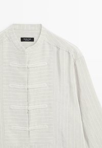 Jasnoszara bawełniana koszula na guziki z kołnierzem typu mandarynka, z pionowymi paskami i pięcioma guziczkami ozdobionymi w kształcie żabek z przodu.