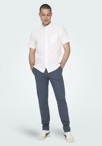 Camisa blanca de manga corta con un bolsillo en el pecho, combinada con pantalones azul oscuro ajustados y zapatillas blancas con detalles en negro.