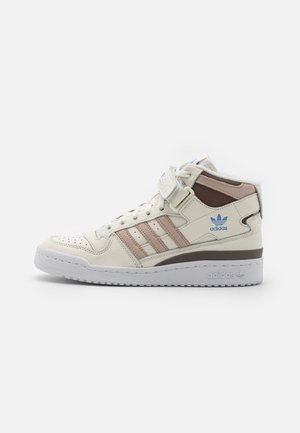 Baskets montantes Adidas crème avec des rayures beige, logo bleu, bride velcro et semelle blanche, vues de profil sur fond blanc.