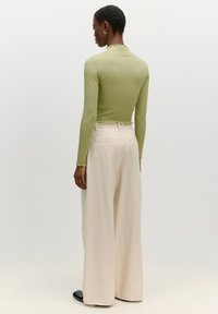 Langarm, lichtgroen top met een gegolfde halslijn, gecombineerd met brede, crèmekleurige broek. Soepele textuur, ontspannen pasvorm, minimale details.
