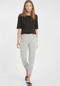 Top corto nero a maniche corte abbinato a pantaloni grigi chiari a gamba affusolata con tasche laterali con zip, tessuto liscio e design aderente.
