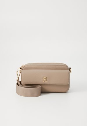 Beżowa prostokątna torba na ramię z złotym emblematem logo, przednią kieszenią na klapie, zamknięciem na suwak u góry oraz szerokim, regulowanym paskiem na ramię.