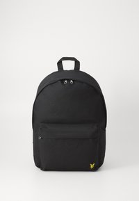 Sac à dos en tissu noir de forme arrondie, avec un compartiment principal zippé, une poche avant et un petit logo jaune en bas à l'avant.