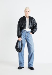 Black cropped leather jacket with ribbed cuffs, light grey top, blue high-waisted jeans, and black chunky boots, holding a textured black bag.