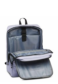 Mochila de color púrpura claro con un bolsillo frontal con cremallera, dos compartimentos, cremalleras negras y un asa de cinta en la parte superior. Textura de tela suave.
