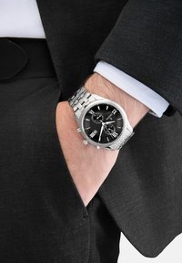 Edelstahlarmbanduhr mit schwarzem Ziffernblatt, silberfarbenen Markierungen, Chronographenfunktion und einem verbundenen Metallarmband, getragen an einem eleganten Handgelenk.